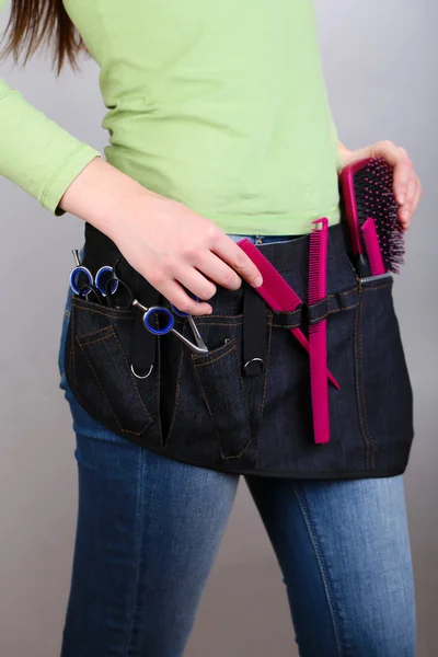 Peluquería mujer con cinturón de herramientas sobre fondo gris — Foto de Stock