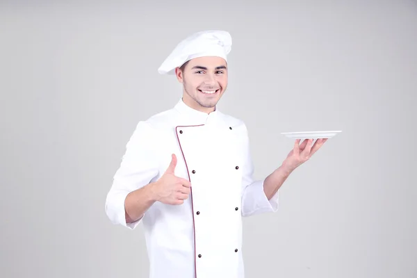 Professionele chef-kok in het witte uniform en hoed, op grijze achtergrond — Stockfoto