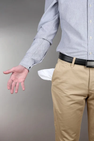 Hombre mostrando su bolsillo vacío sobre fondo gris —  Fotos de Stock