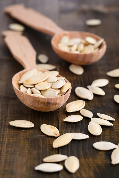Pumpkin seeds in spoons on wooden background — Stock Photo, Image