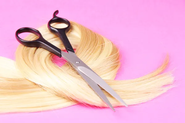 Long blond hair with scissors on pink background — Stock Photo, Image