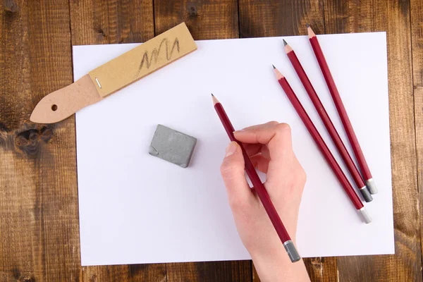 Hand hält Bleistift mit Kunstmaterialien auf Holzgrund — Stockfoto