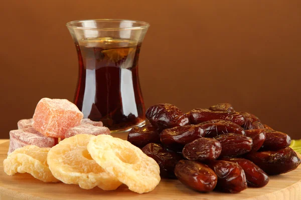 Dried dates with cup of tea and sweets on table on brown background — Stock Photo, Image