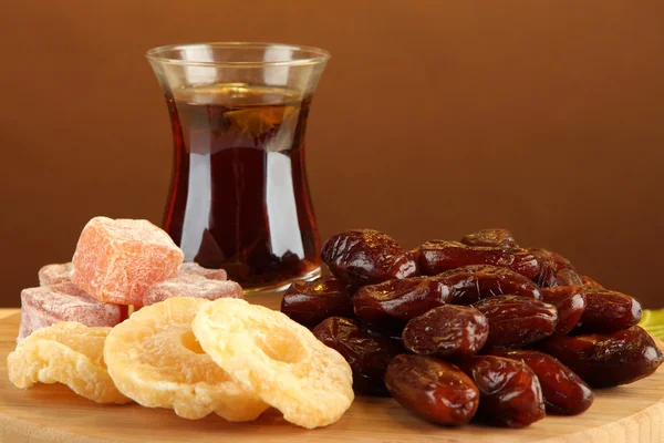 Date secche con tazza di tè e dolci sul tavolo su sfondo marrone — Foto Stock