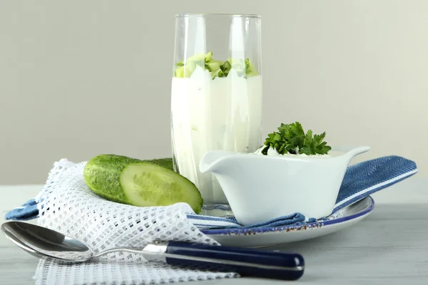 Iogurte de pepino em vidro, em guardanapo de cor, em mesa de madeira, em fundo cinza — Fotografia de Stock