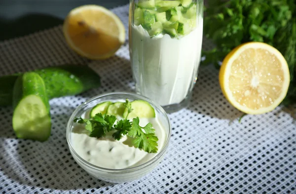 Yogurt al cetriolo in vetro e ciotola, su tovagliolo di colore, su tavola di legno, su sfondo scuro — Foto Stock