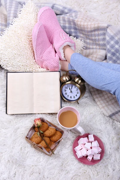 Komposition mit warmem Karo, Buch, Tasse Heißgetränk und weiblichen Beinen, auf farbigem Teppich Hintergrund — Stockfoto