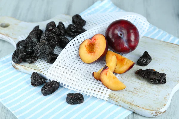 Fresh and dried plums on napkin, on wooden background — Stock Photo, Image