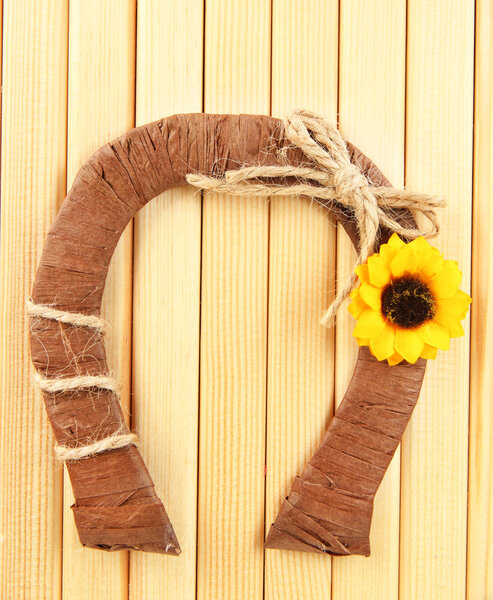 Decorative horseshoe of straw with sunflower, on wooden background