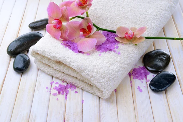 Still life with beautiful blooming orchid flower, towel and bowl with sea salt, on color wooden background — Stock Photo, Image