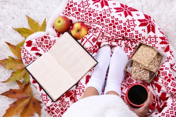 Composição com xadrez quente, livro, xícara de bebida quente e pernas femininas, no fundo do tapete de cor — Fotografia de Stock