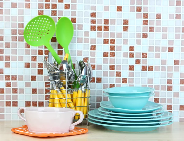 Platos y cubiertos en la cocina en la mesa en el fondo de azulejos de mosaico — Foto de Stock