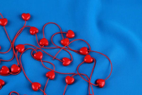 Korálky ve tvaru srdce na řetězec na pozadí tkaniny — Stock fotografie