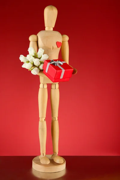 Wooden mannequin holding gift box and bouquet on red background — Stock Photo, Image