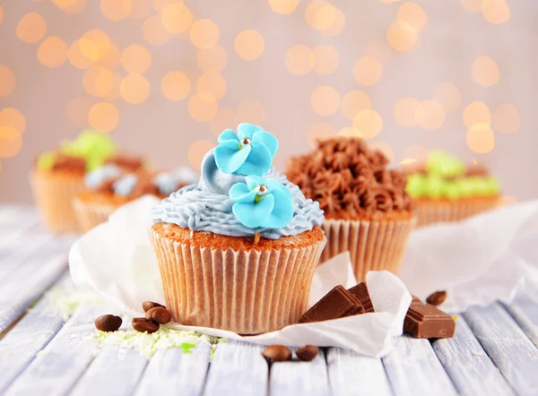 Sabrosos cupcakes con crema de mantequilla, sobre tabla de madera de color, sobre fondo de luces — Foto de Stock