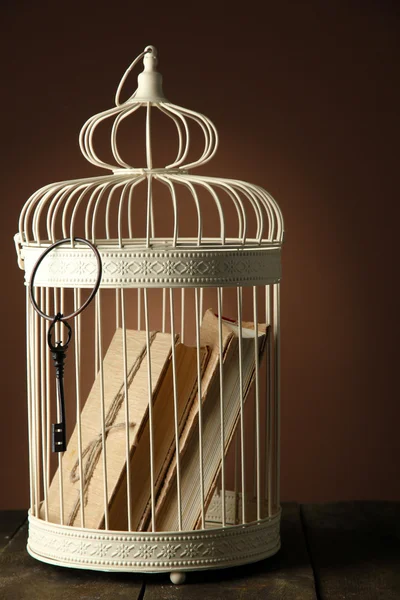 Books in decorative cage on wooden table, brown on background — Stock Photo, Image