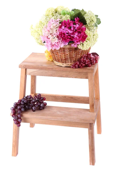 Cesta de mimbre con flores y frutas, en una pequeña escalera de madera, aislada en blanco —  Fotos de Stock