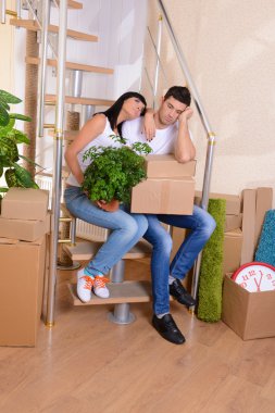 Young couple with boxes in new home on staircase background clipart