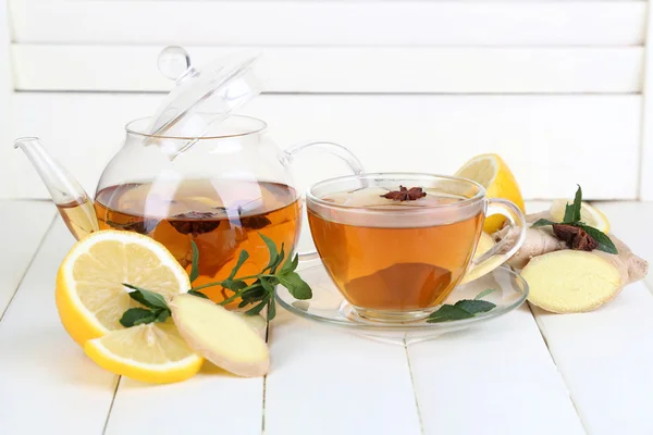 Wasserkocher und Tasse Tee mit Ingwer auf Holztisch auf hellem Hintergrund — Stockfoto