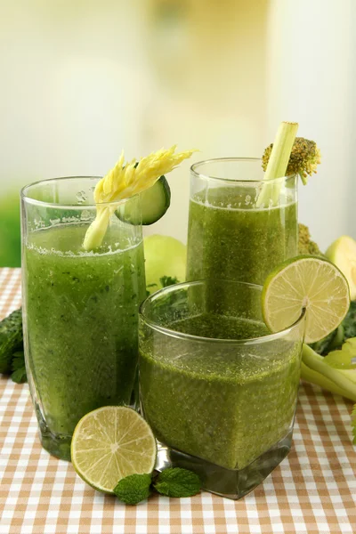 Bicchieri di succo vegetale verde e verdure su tovaglia su sfondo brillante — Foto Stock