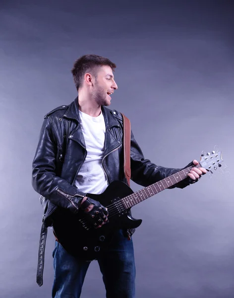 Jovem músico tocando guitarra em fundo cinza — Fotografia de Stock