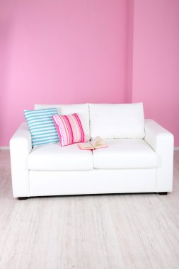 Odada pembe bir arka plan üzerinde beyaz kanepe