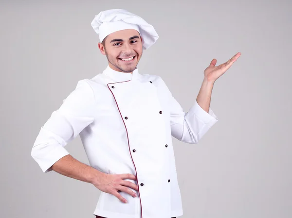 Chef profesional en uniforme blanco y sombrero, sobre fondo gris — Foto de Stock