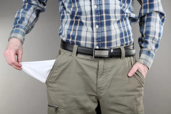 Hombre mostrando su bolsillo vacío sobre fondo gris — Foto de Stock