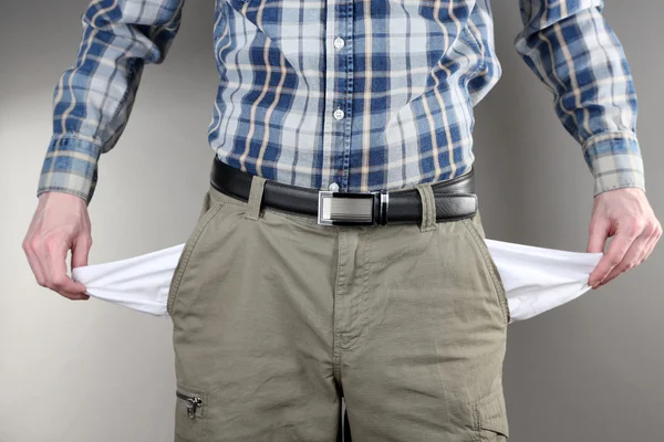 Muž ukazuje prázdný kapsy na šedém pozadí — Stock fotografie