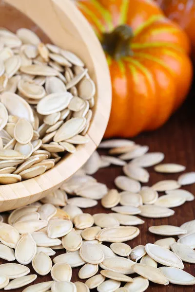 Pumpkin seeds in bowl with pumpkin on table close up — Stock Photo, Image