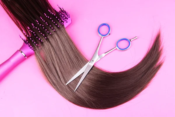 Cabelo castanho longo com escova de cabelo e tesoura sobre fundo rosa — Fotografia de Stock