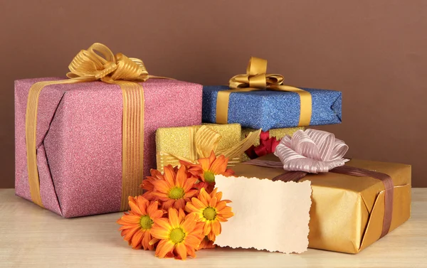 Caixas de presente com etiqueta em branco e flores na mesa sobre fundo marrom — Fotografia de Stock