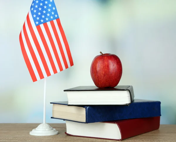 Sammansättningen av amerikanska flaggan, böcker och äpple på träbord, på ljus bakgrund — Stockfoto