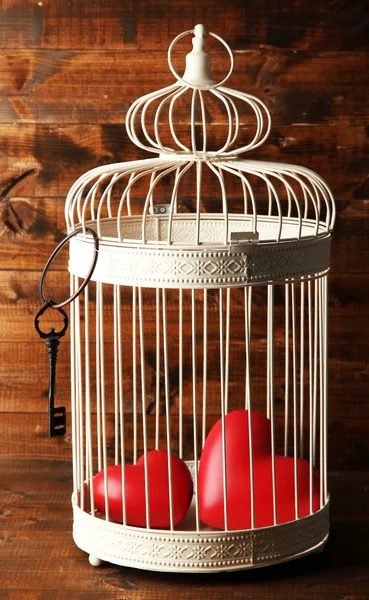 Hearts in decorative cage on wooden background — Stock Photo, Image
