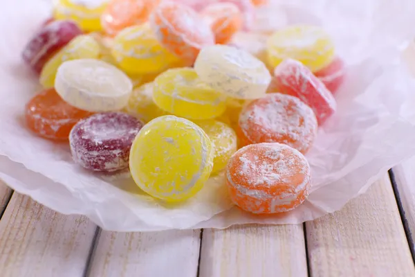 Sweet multicolor candies on paper, on color wooden background — Stock Photo, Image