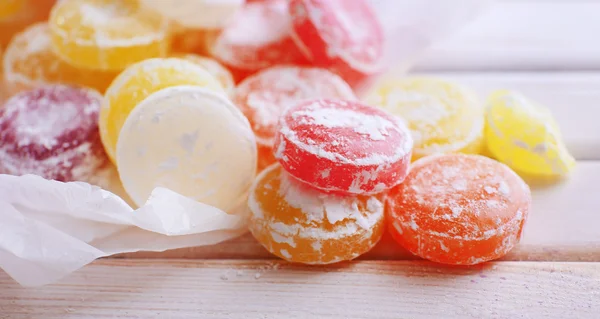 Dolci caramelle multicolore su carta, su sfondo di legno a colori — Foto Stock