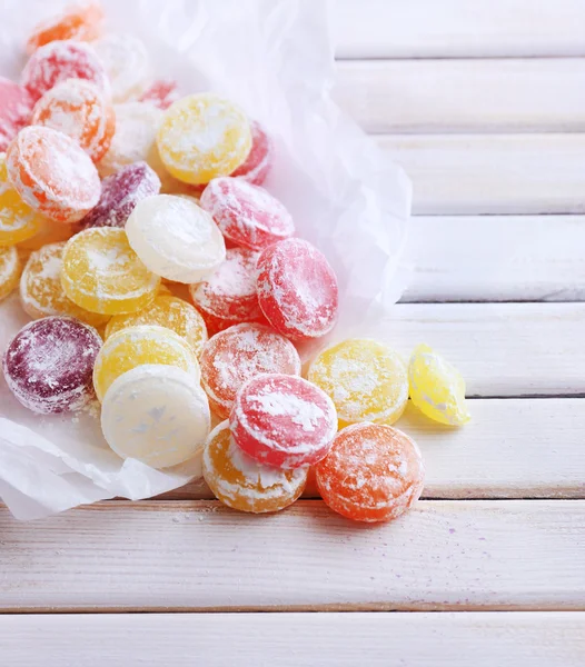 Sweet multicolor candies on paper, on color wooden background — Stock Photo, Image