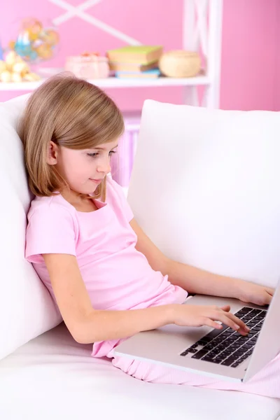 Bambina seduta con computer portatile sul divano in camera — Foto Stock