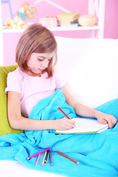 Dziewczynka rysuje, siedząc na kanapie w pokoju — Zdjęcie stockowe
