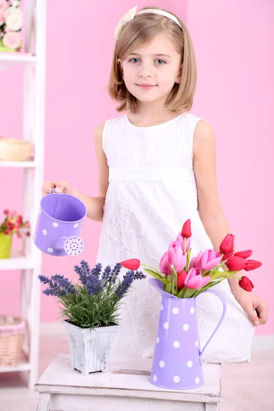 Beautiful little girl and stand with flowers on pink background — Stock Photo, Image