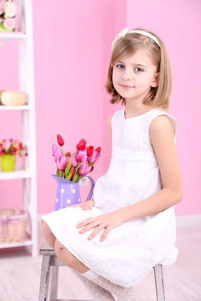 Little girl sitting on small ladder with flowers on pink background — Stock Photo, Image