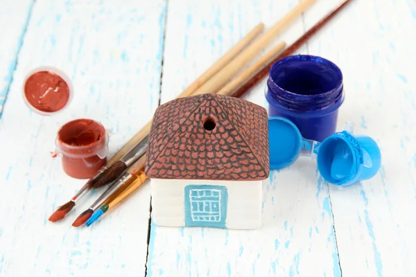 Hand made ceramic house and color paints on wooden table — Stock Photo, Image