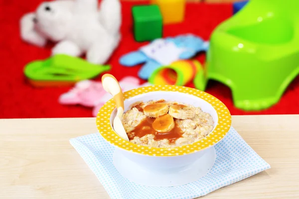 Tigela de mingau de cereal para bebê e brinquedos na mesa, no fundo de brinquedos — Fotografia de Stock