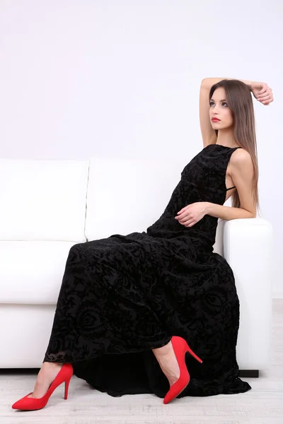 Mulher bonita em vestido preto no sofá no fundo branco — Fotografia de Stock