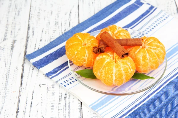 Ripe sweet tangerines with spices on color plate, on napkin, on wooden background — Stock Photo, Image