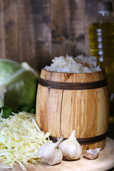 Composition with fresh and marinated cabbage (sauerkraut) in wooden barrel, on wooden table background