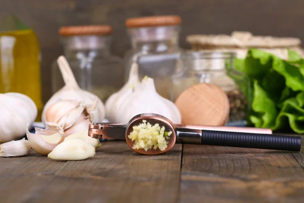 Composition with garlic press, fresh garlic and glass jars with spices on wooden background — Stock Photo, Image