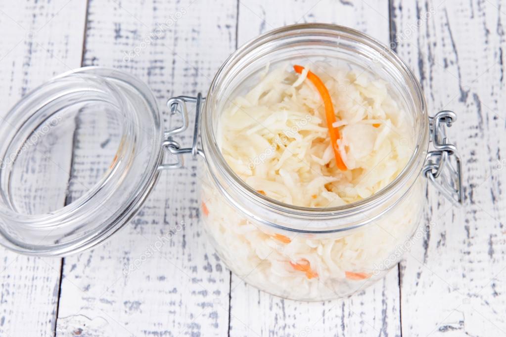 Marinated cabbage (sauerkraut) in glass jar, on wooden background