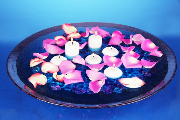 Rose petals and candles in water in vase on blue background close-up — Stock Photo, Image