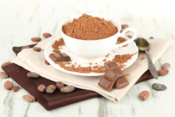 Cocoa powder in cup on napkin on wooden table — Stock Photo, Image